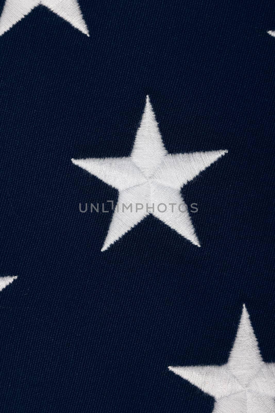 Close up embroidered white stars on blue canton of heavy cotton canvas US national flag, symbol of American patriotism, elevated high angle view, directly above