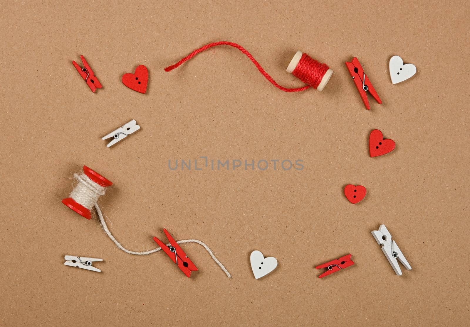 Frame of Valentine gift decorations, twine, clothespins and hearts over brown paper background, close up flat lay, elevated top view, directly above