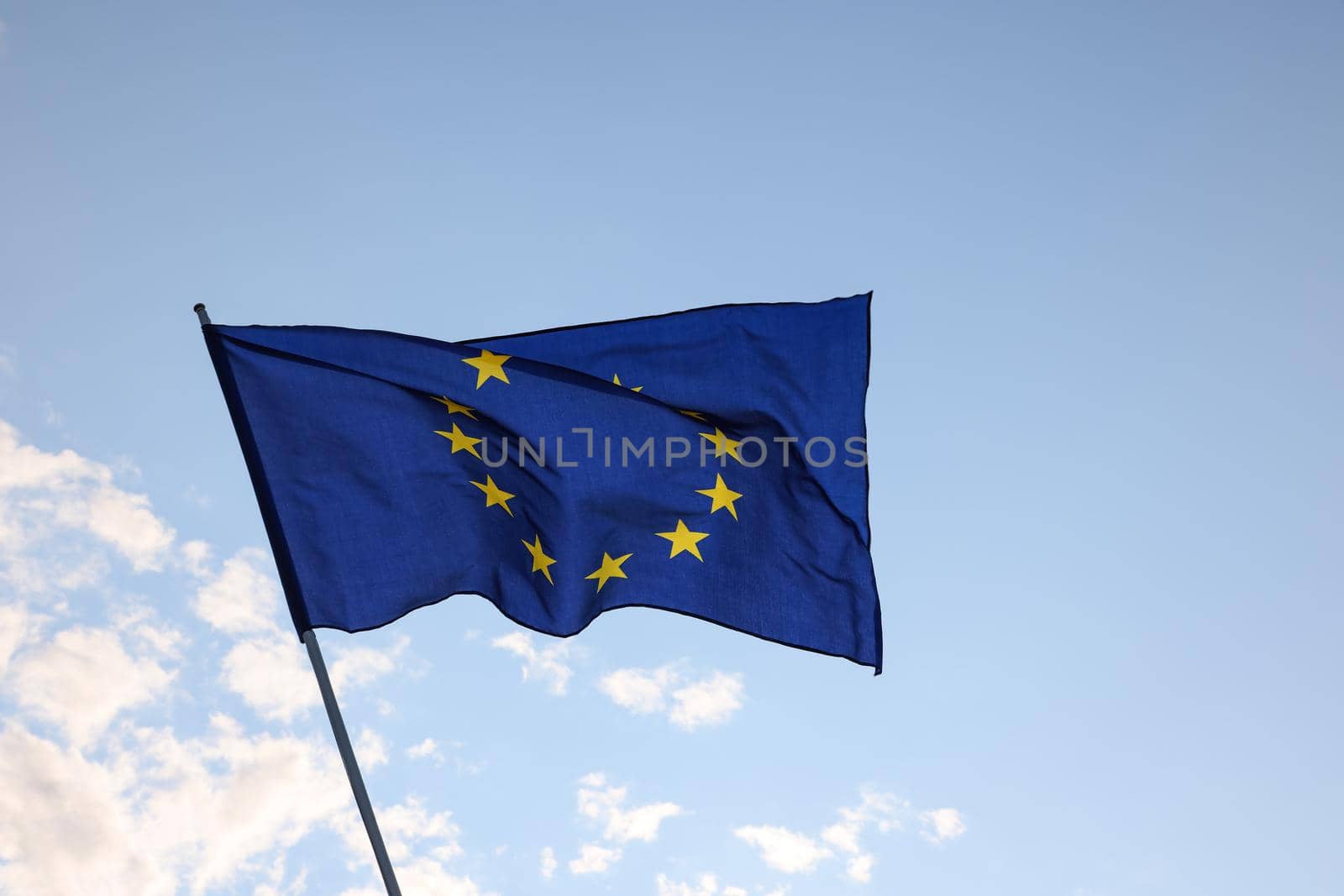 European Union EU flag flying and waving in the wind over clear blue sky, symbol of European patriotism, low angle, side view