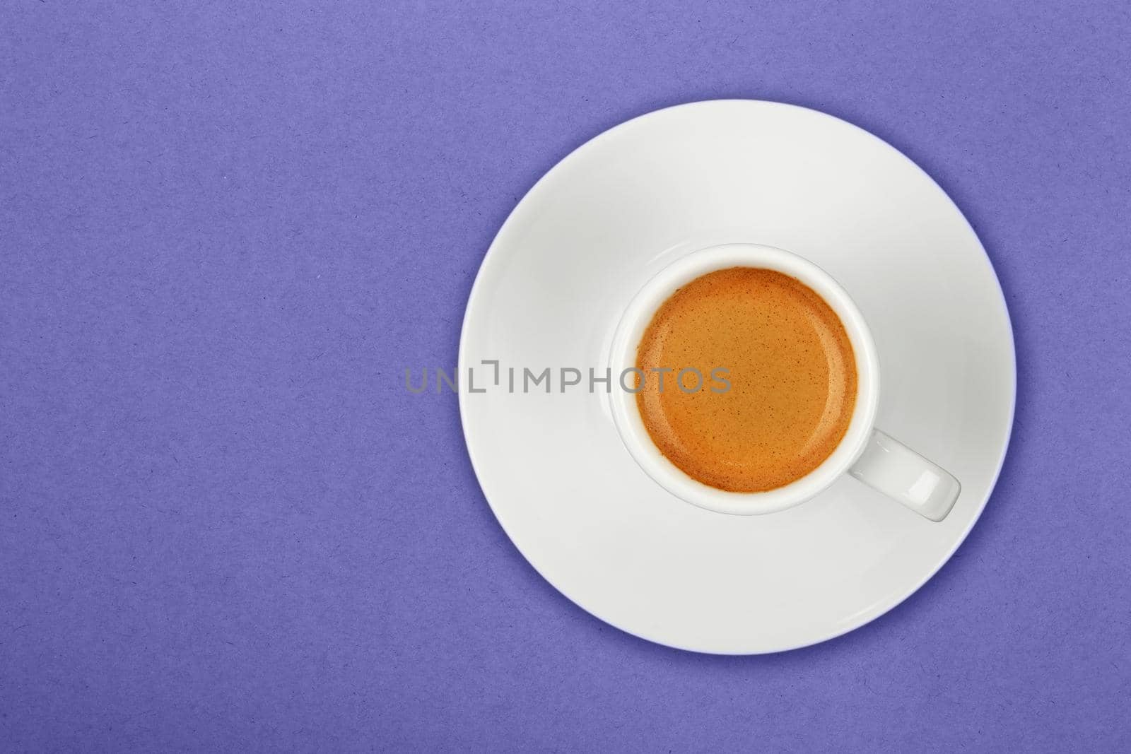 Close up one white cup full of espresso coffee on saucer over lavender background, very peri, color of year 2022, elevated top view, directly above