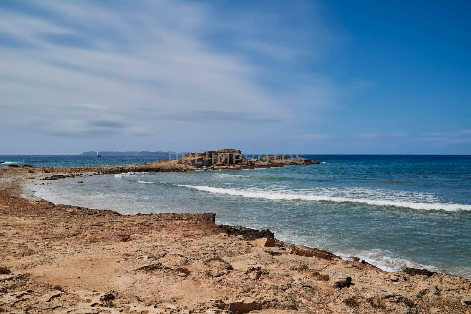 Mediterranean rocky beach. Small waves, rocky cove, sky with few white clouds. Balearic Islands