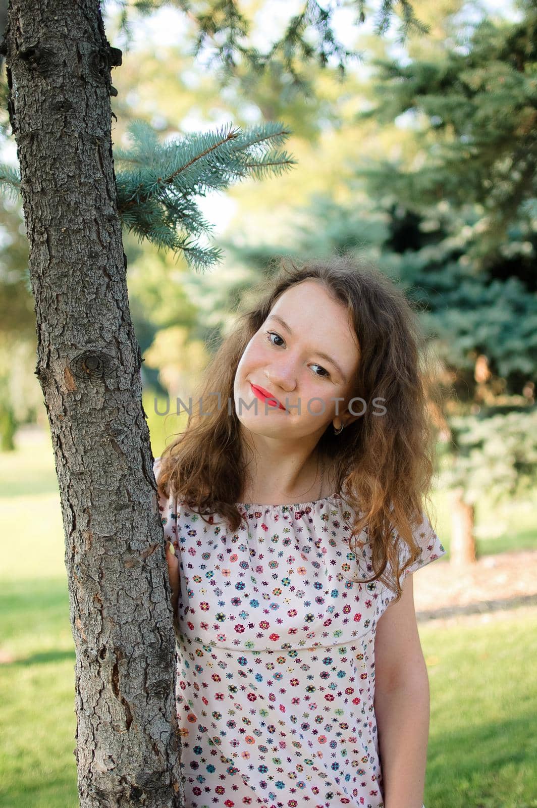 Young brunette girl in dress is posing on tree background in the summer in park.