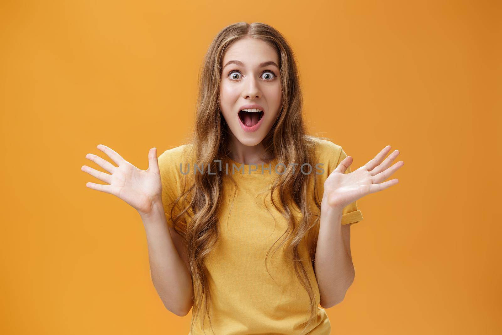 Impressed excited girl describing feelings sharing positive impression gesturing with palms during talk open mouth from amazement and oy communicating lively over orange background by Benzoix