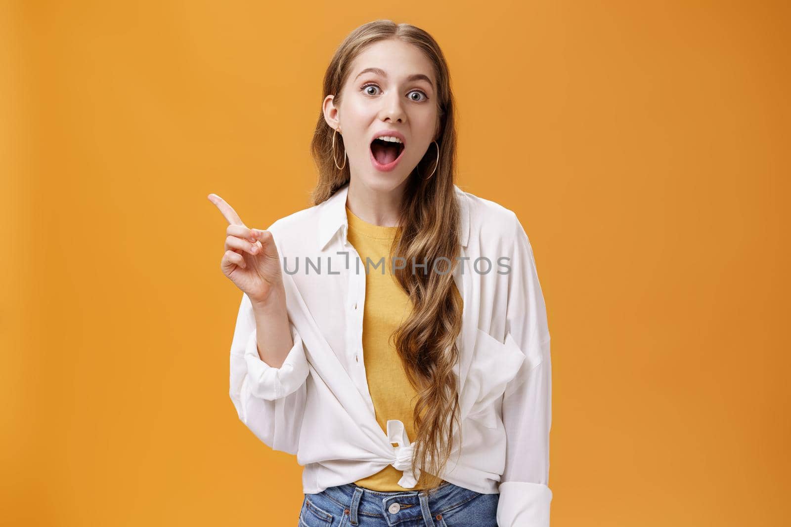 Your jaw will drop after this copy space. Portrait of charismatic young good-looking stylish girl with wavy hair open mouth widely pointing at upper left corner showing awesome place or product by Benzoix