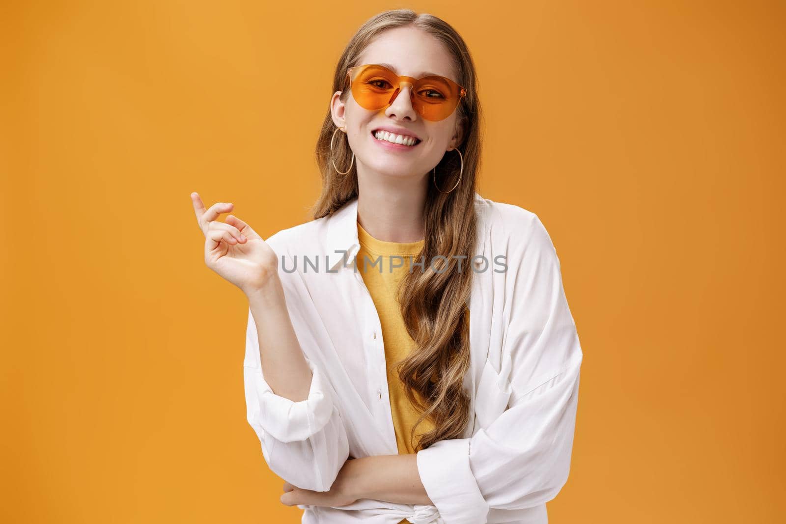 Sunglasses matching style. Portrait of confident and carefree good-looking female fashion blogger in eyewear and white t-shirt gesturing with raised hand and smiling cheerfully at camera.