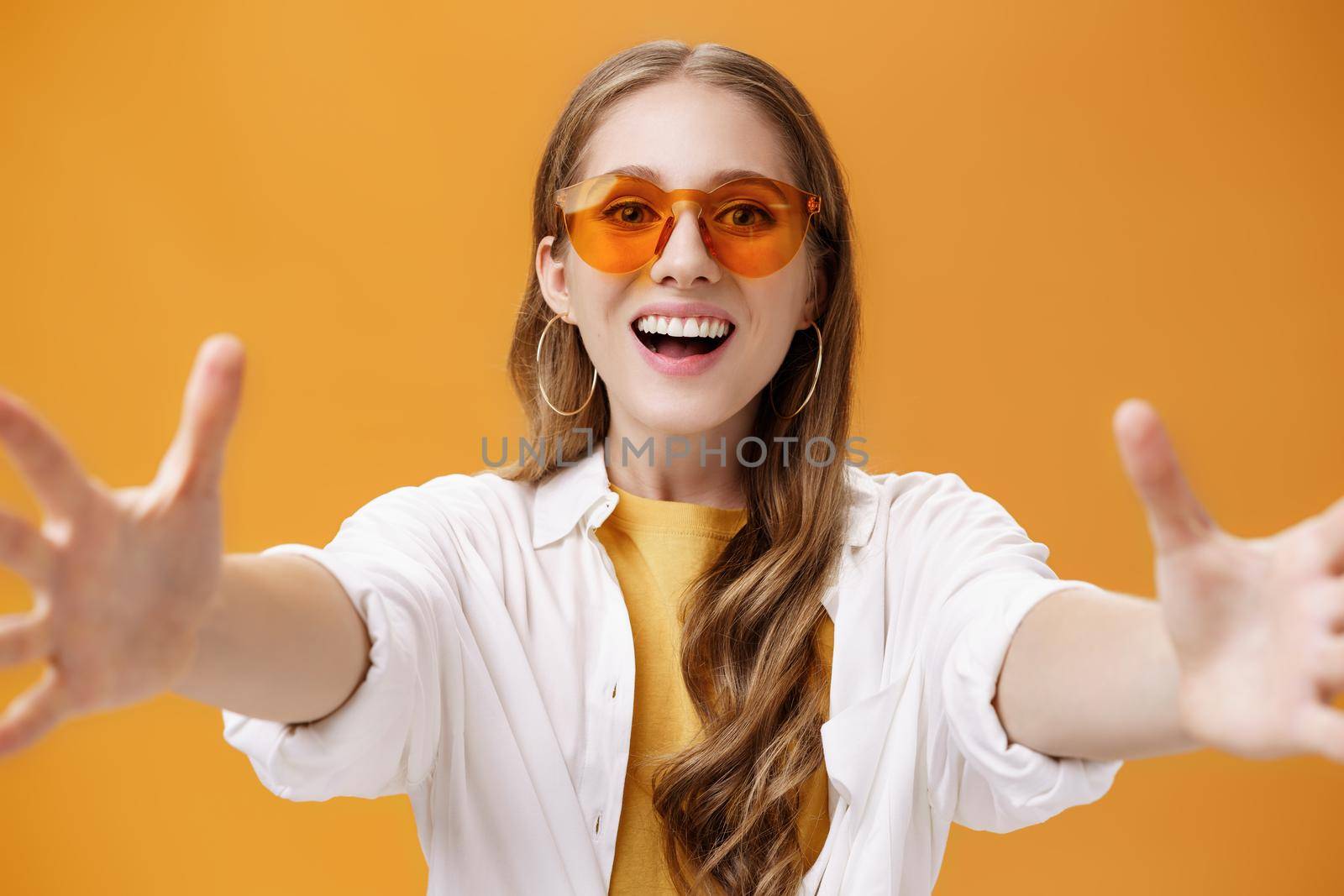 Lifestyle. Girl reaching to camera to hug or grab thing looking forward with broad grin and excited desiring expression wanting hold in hands new product posing amused and happy over orange background.