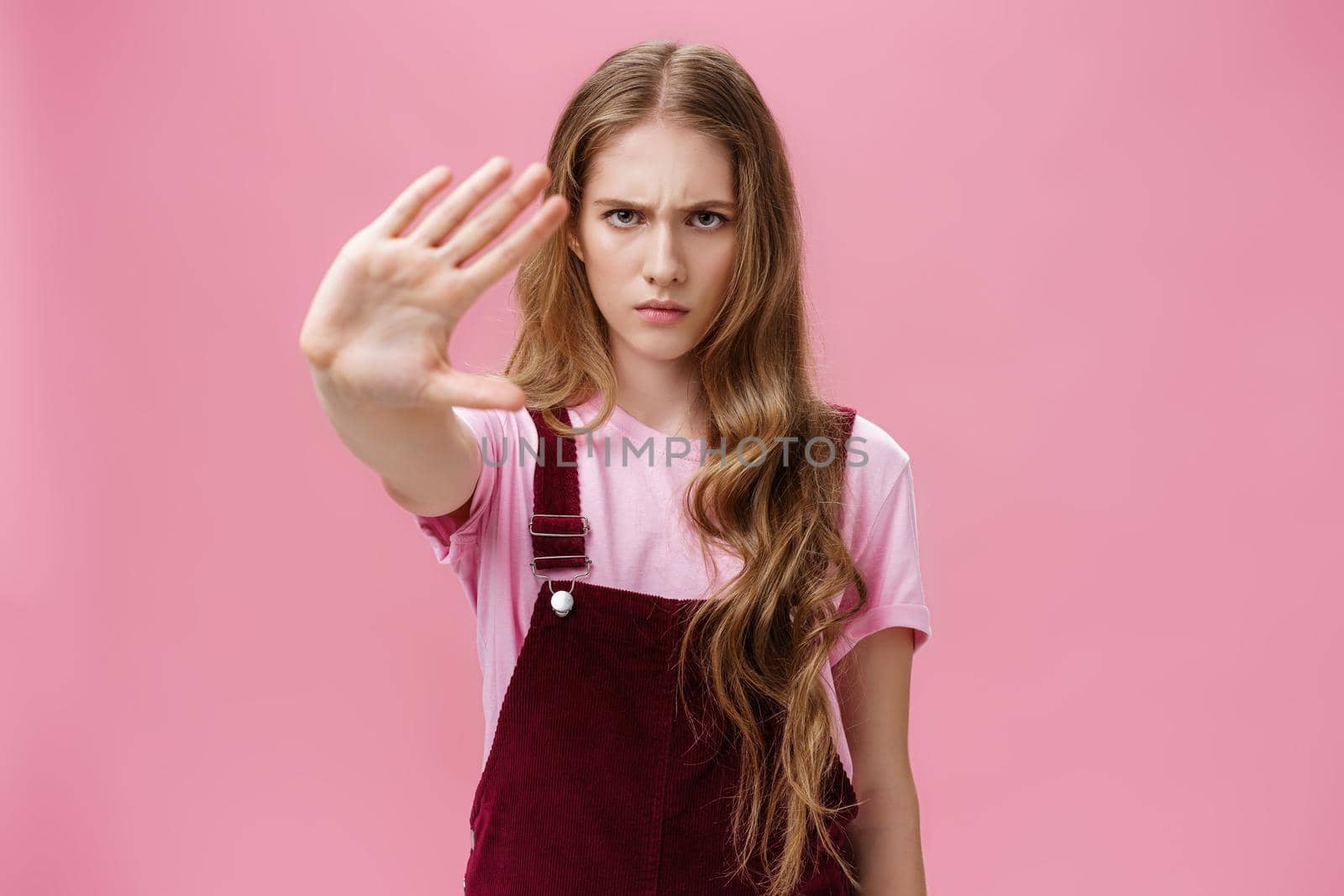 Woman protest against testing products on animals. Serious-looking confident young girl with long wavy hair frowning looking sctrict at camera pulling palm towards camera in prohibition and no gesture. Body language concept