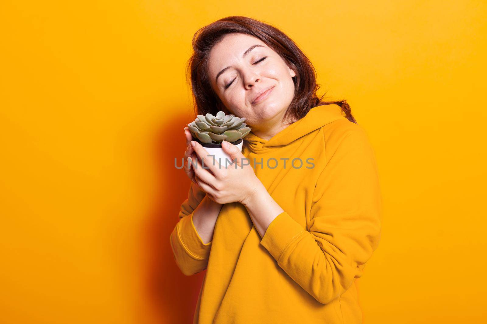 Positive woman holding pot with green plant in hand. Caucasian person taking care of houseplant with leafs for natural decoration. Gardener with vegetation object of botany and flora