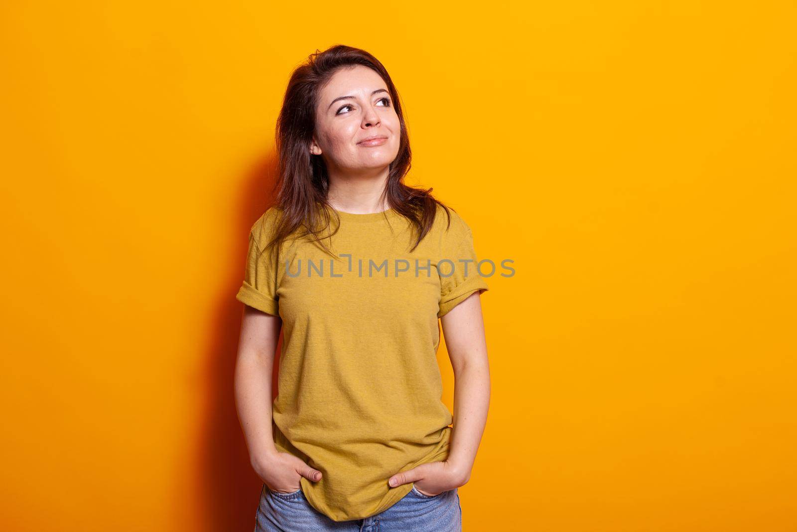 Portrait of caucasian woman standing in studio and smiling, looking at side. Young adult feeling happy and carefree over isolated background in front of camera. Joyful casual person