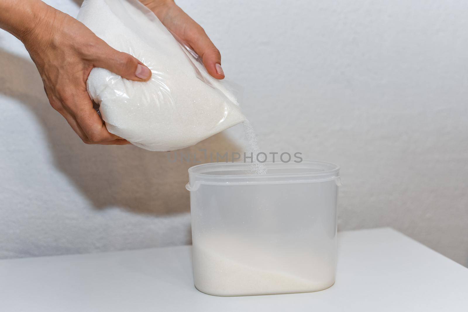 Storing sugar at home, arranging a place in the kitchen. Pouring sugar from a bag into a plastic container.