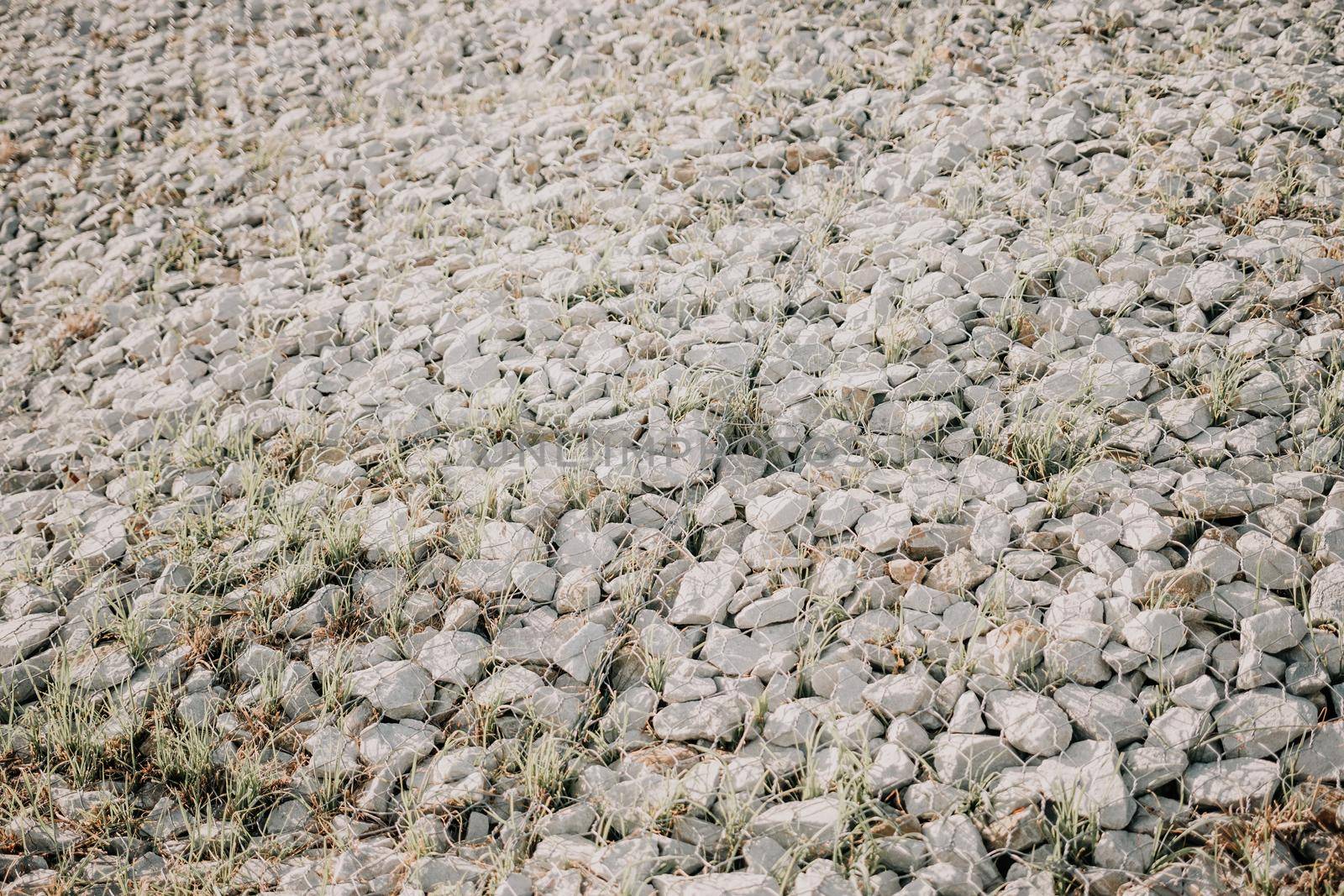 strengthening the slope with stones behind the wire. grey texture. construction. Granite stones behind a metal grate