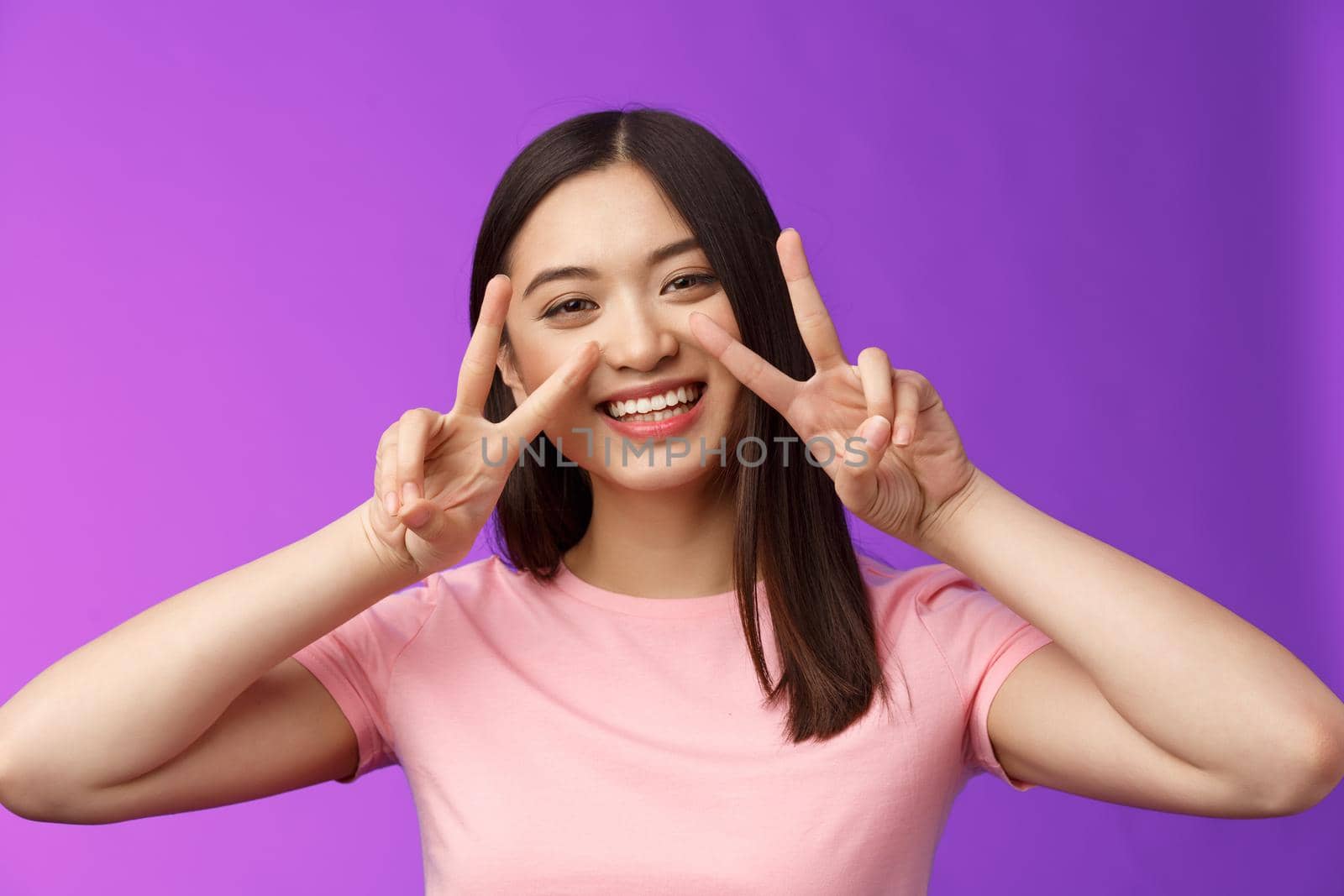 Close-up friendly positive outgoing nice asian girl show peace, victory signs cherish friendhsip stay optimistic, smiling broadly, having funny summer holidays, stand purple background.