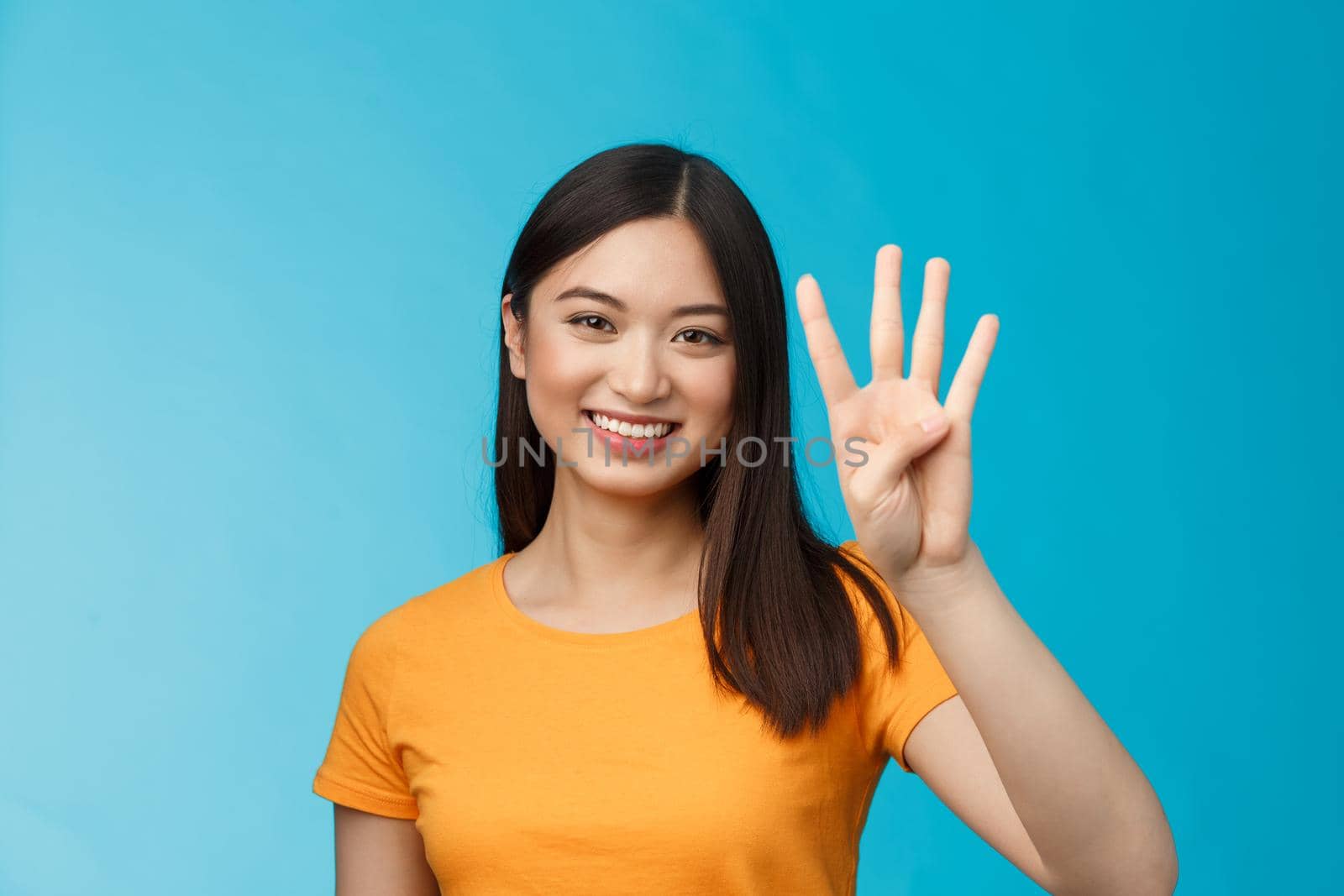 Close-up charismatic tender stylish asian female show number four fingers, smiling happily, making order, explain how much items want buy, stand blue background carefree. Copy space
