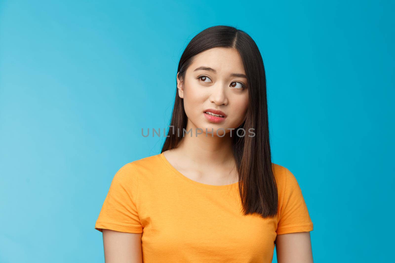 Doubtful unsure cute asian girl dark short haircut look left questioned, see strange thing, open mouth frowning upset uncertain, have hesitations, peek suspicious aside, stand blue background by Benzoix