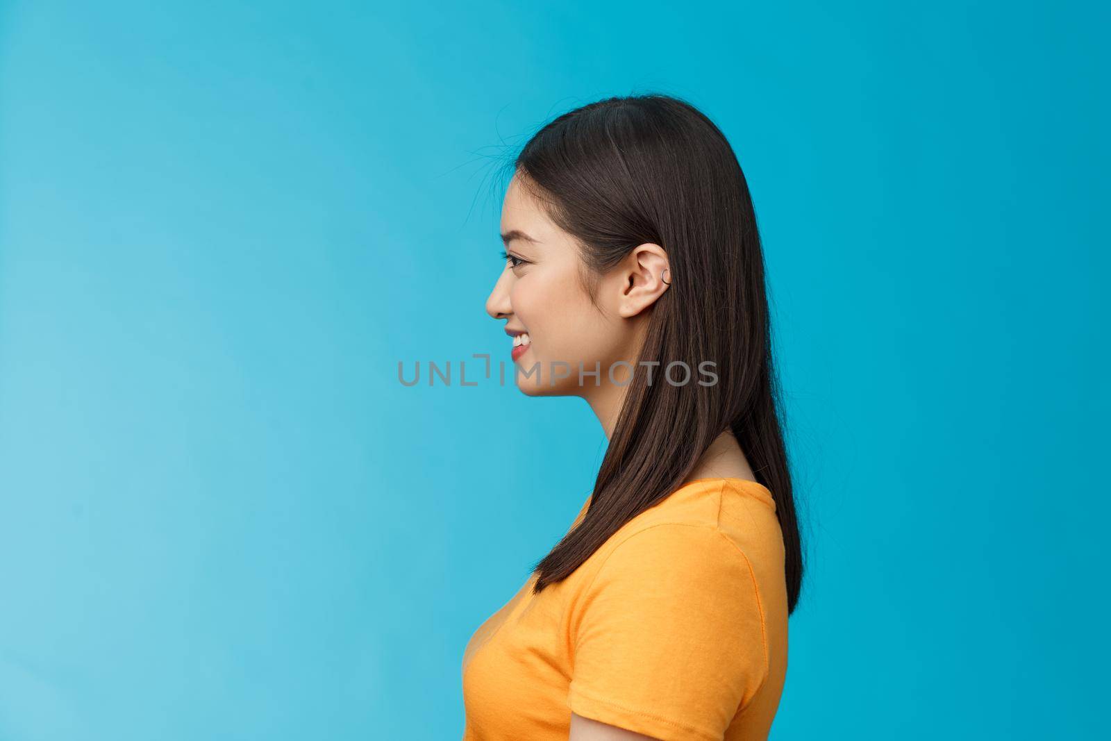 Profile shot asian cute woman perfect skin, turn left, smiling joyfully, pose near blue background, standing queue, awaiting coffee take-away, relaxed chatting girlfriend, wear yellow summer t-shirt by Benzoix