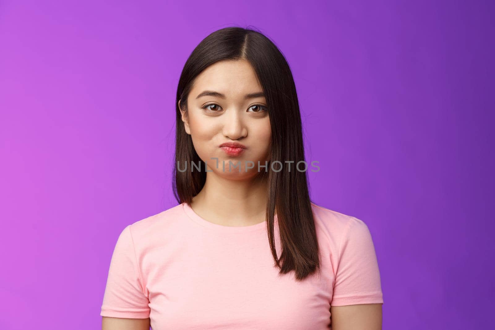 Close-up cute tender young asian female holding breath speechless, smiling silly having challenge hiding secret unwilling talk, pouting lovely, look camera entertained, purple background.
