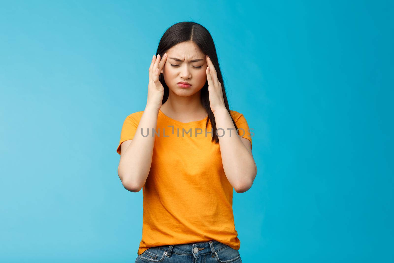 Distressed tired asian woman dark haircut cringe touch temples, suffer huge migraine need painkillers, painful headache, feel dizzy, stand blue background intense drained. Copy space