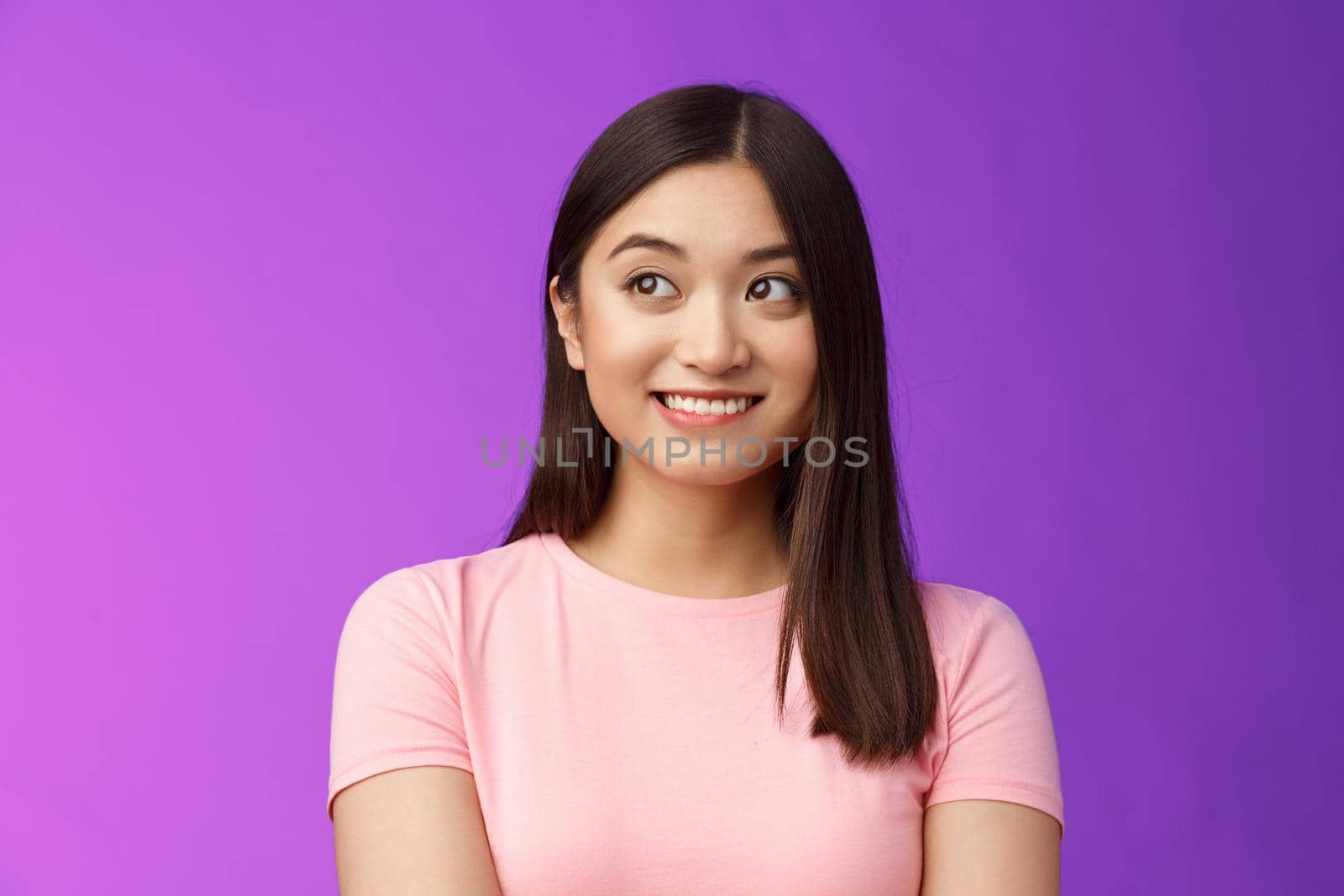 Close-up lovely joyful asian woman look away dreamy, smiling imaging cute thing, recall funny joke, thinking happy moment, stand modest purple background upbeat and silly. Copy space
