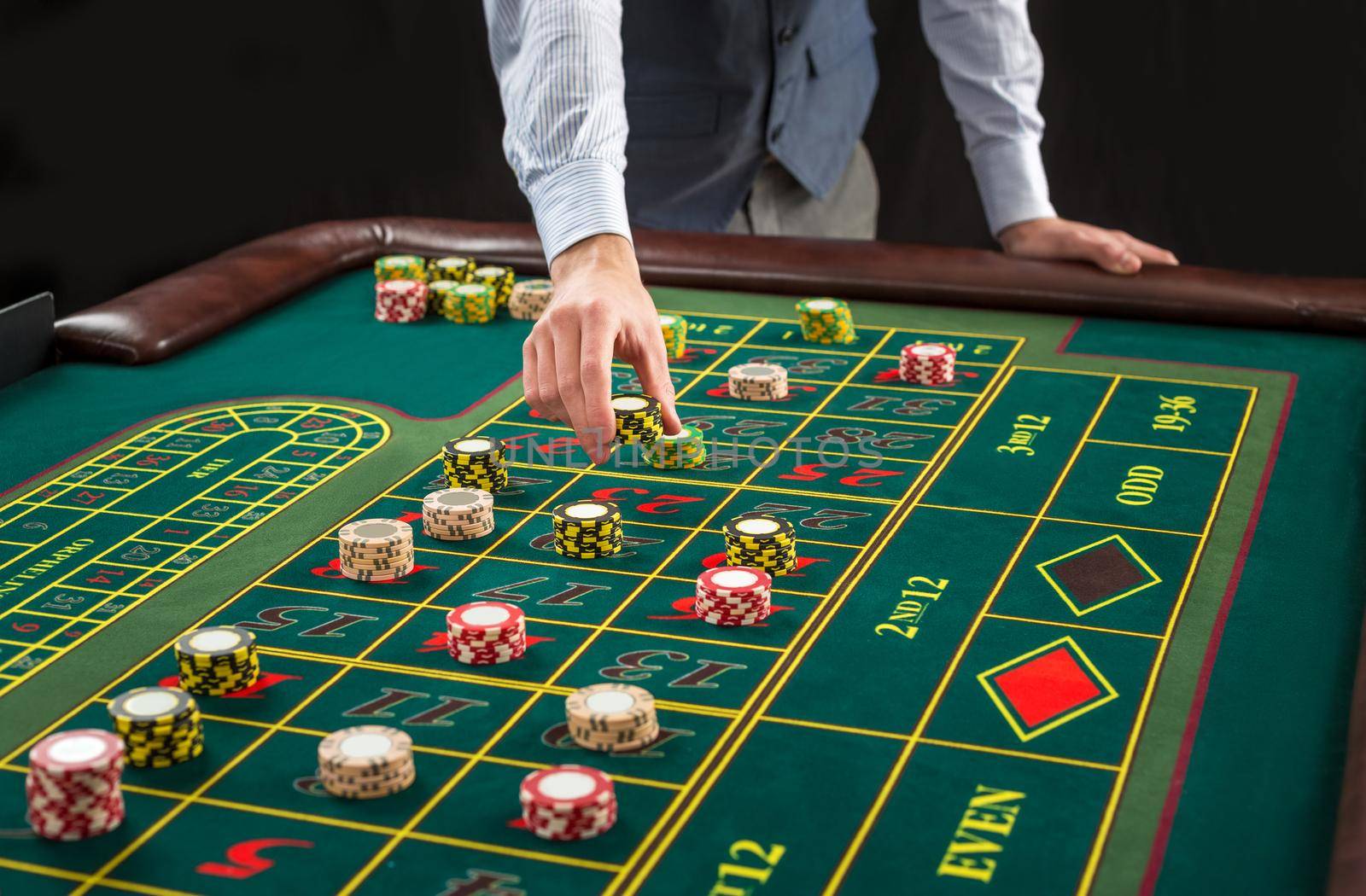 Picture of a green table and betting with chips. Man hand over casino chips on roulette table. Close up