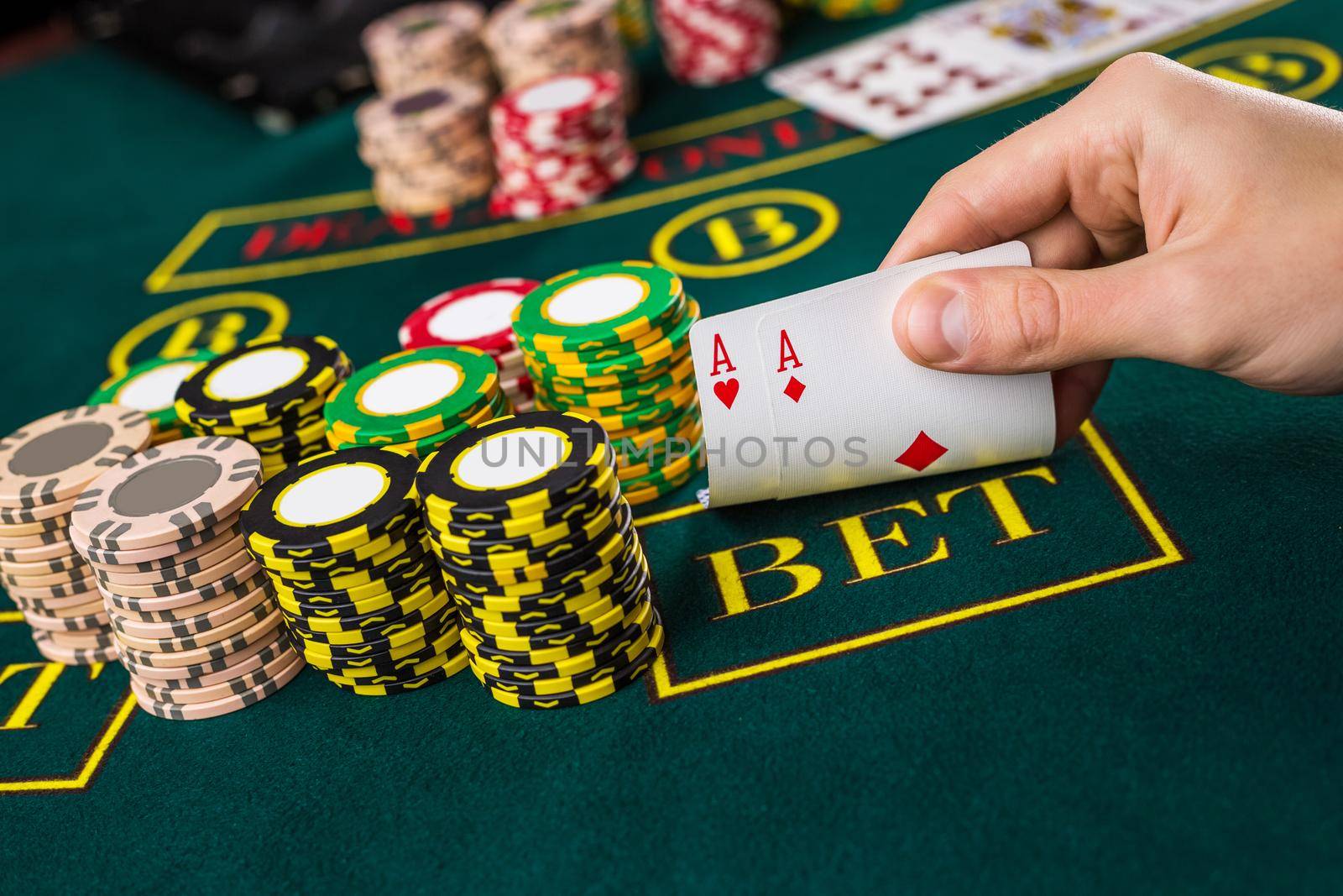 Close-up of male poker player lifting the corners of two cards aces at green casino table with aces