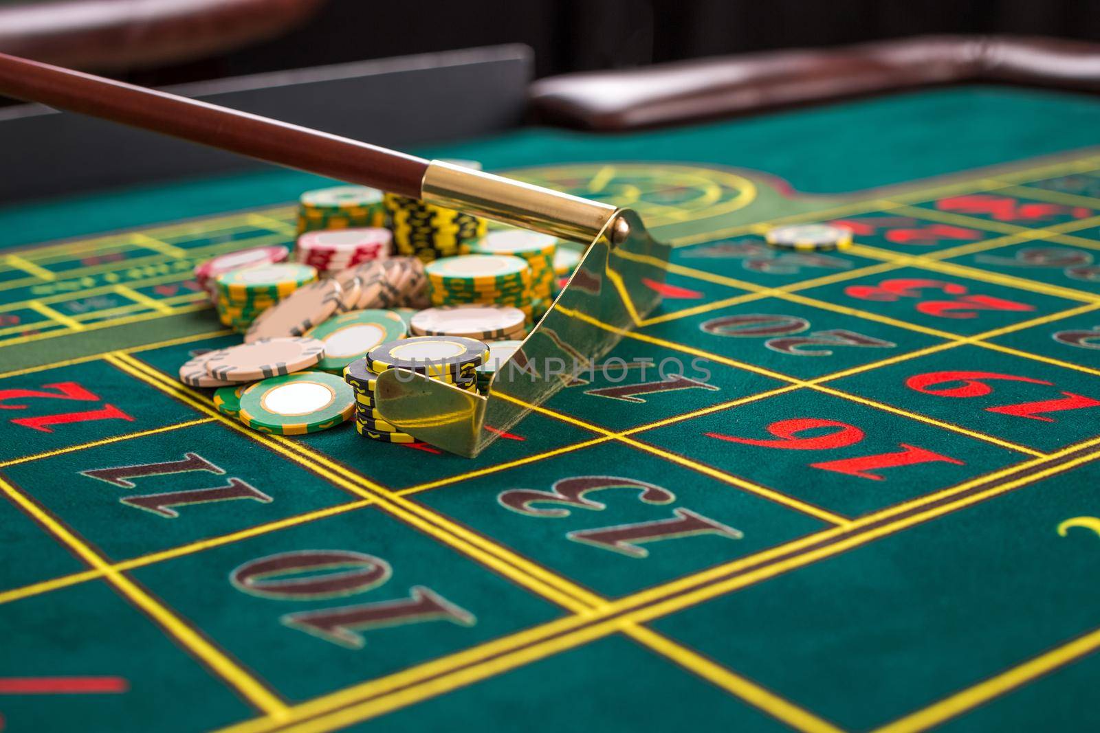 Close up of gambling chips on a green table in casino. Croupier collects chips using stick