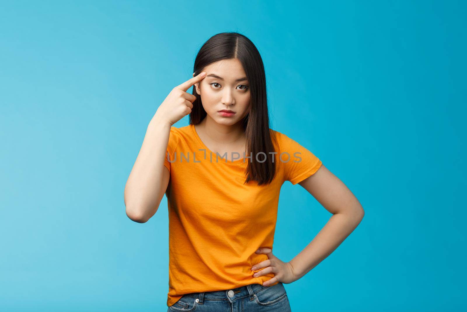 Pissed irritated asian girl look annoyed bend camera roll finger on temple stare camera bothered dismay, asking are you out mind, show person crazy weird, stand blue background by Benzoix