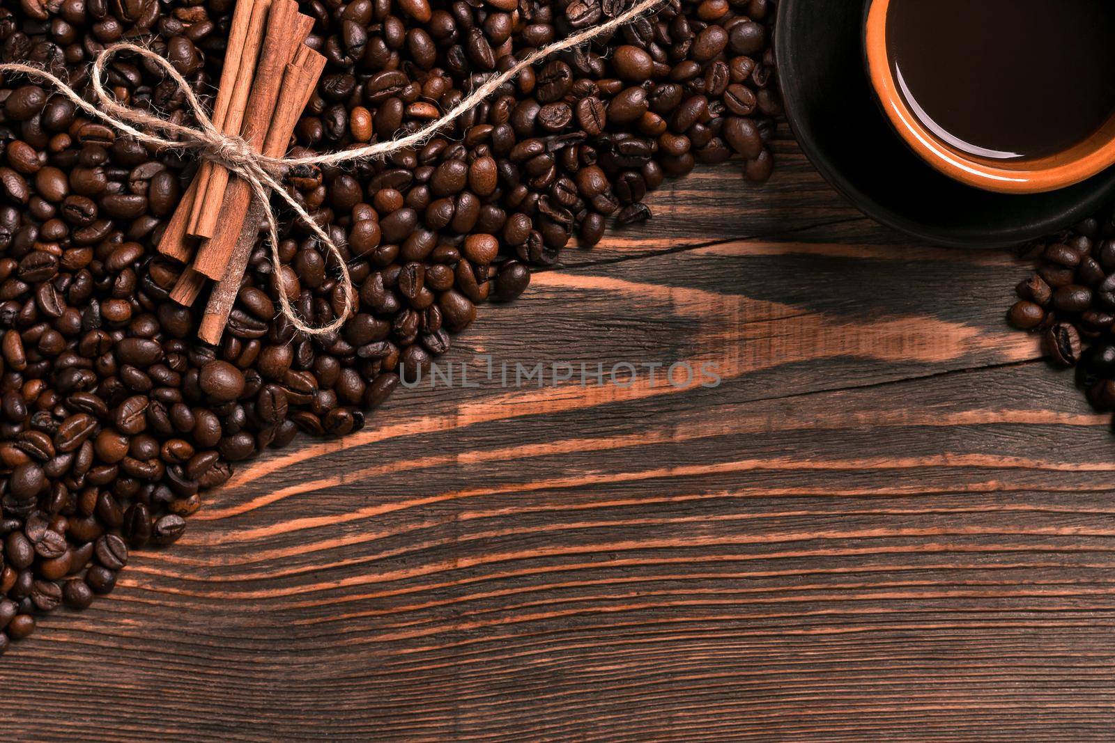 Coffee beans, cinnamon sticks and cup of brewed coffee on rustic wooden table, view from above with space for text. Still life. Mock-up. Flat lay