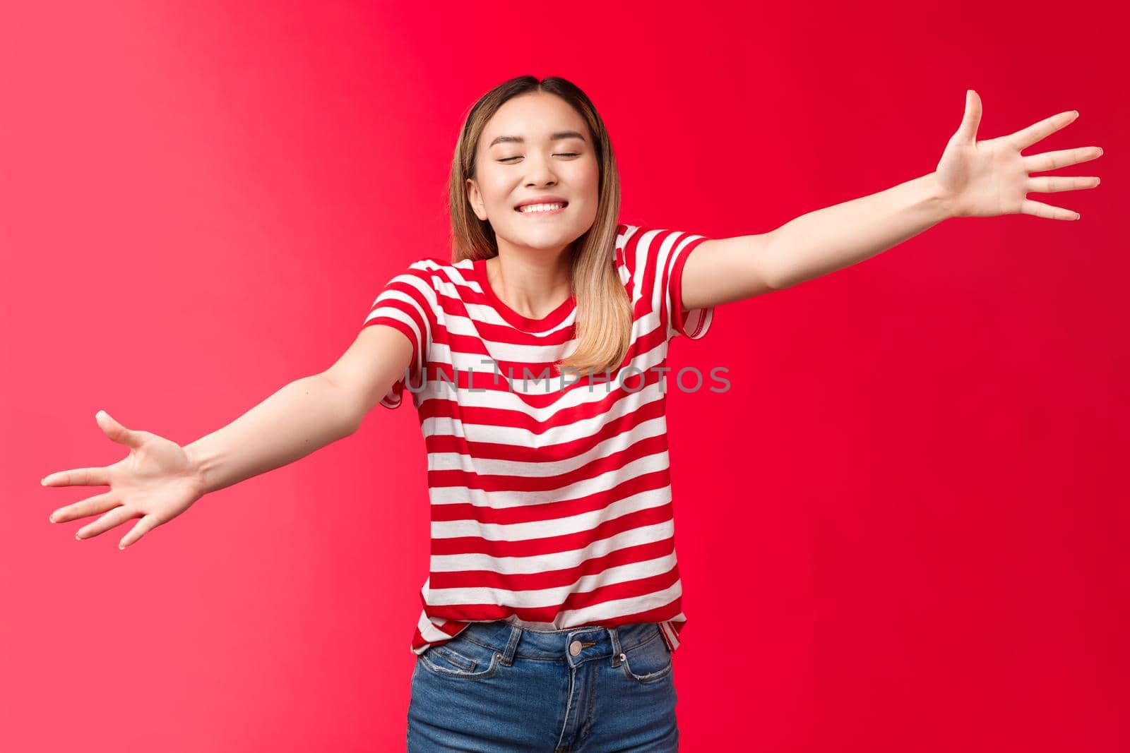 Silly friendly-looking tender blond asian girl close eyes smiling broadly toothy upbeat smile extend arms, wanna give tight hug, reach camera move forward cuddle best friend, red background.