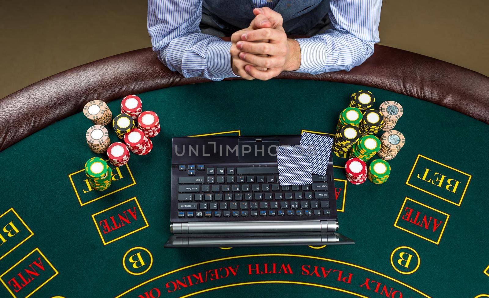 Closeup of poker player with playing cards, laptop and chips by nazarovsergey