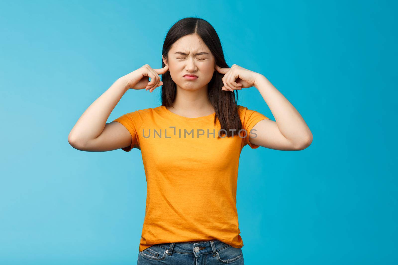 Upset gloomy intense and stressed female student cannot stand loud noises in university dormitory, cringe close ears with index fingers, shut eyes bothered, stand irritated blue background by Benzoix