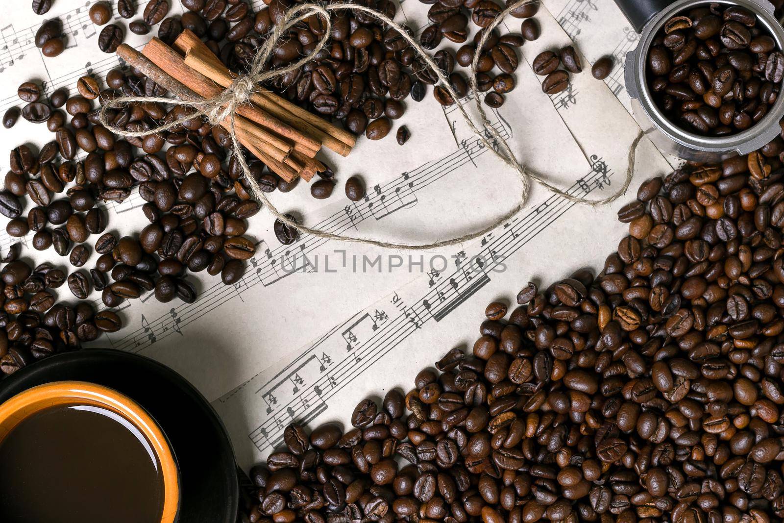 Coffee beans, cinnamon sticks and cup of brewed coffee on sheet music background, view from above with space for text. Still life. Mock-up. Flat lay