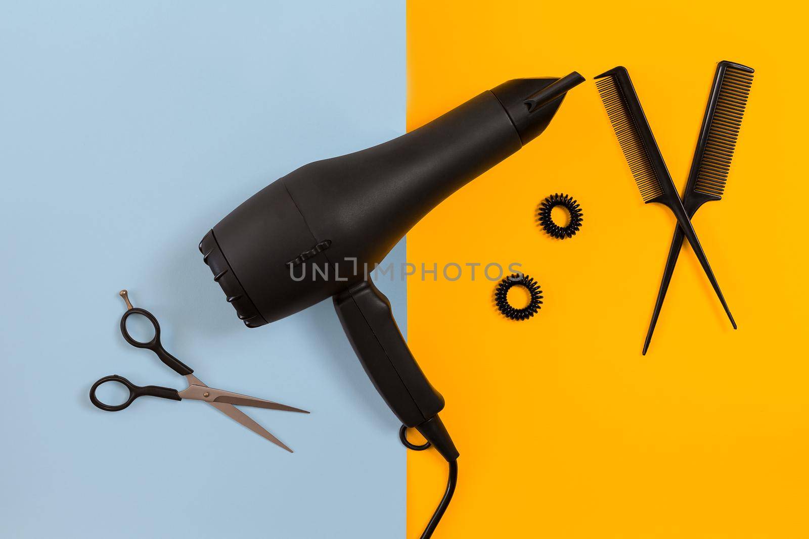 Styling hair with scissors, dryer and tools in barbershop on blue and yellow paper background top view mock-up by nazarovsergey