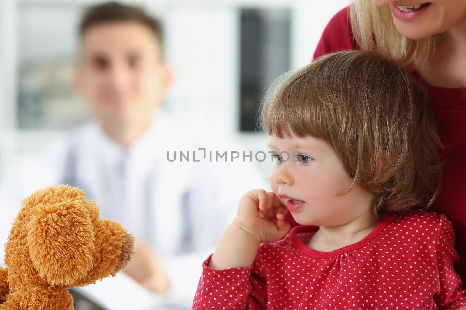 Portrait of little girl with mother play with teddy bear before doctor appointment. Cute child with parent visit family doctor. Hospital, health concept