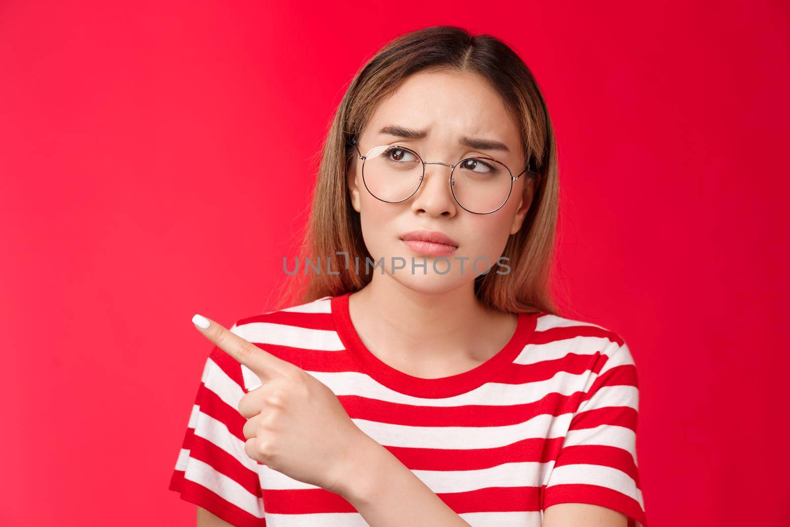 Disappointed doubtful frowning asian girl asking question reassure, looking pointing left displeased, unimpressed with strange place, dislike interiour sulking distressed, stand red background.
