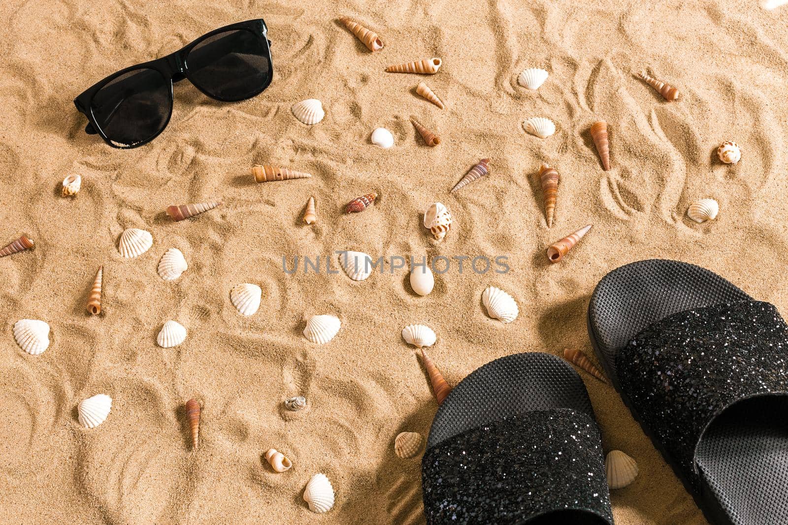 Black flip-flops and sunglass, seashell on sand. With place for your text. Top view. Copy space
