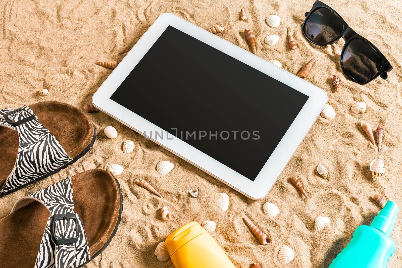 Summer flip-flops, tablet, sunglass and seashell on sand. With place for your text. Top view. Copy space