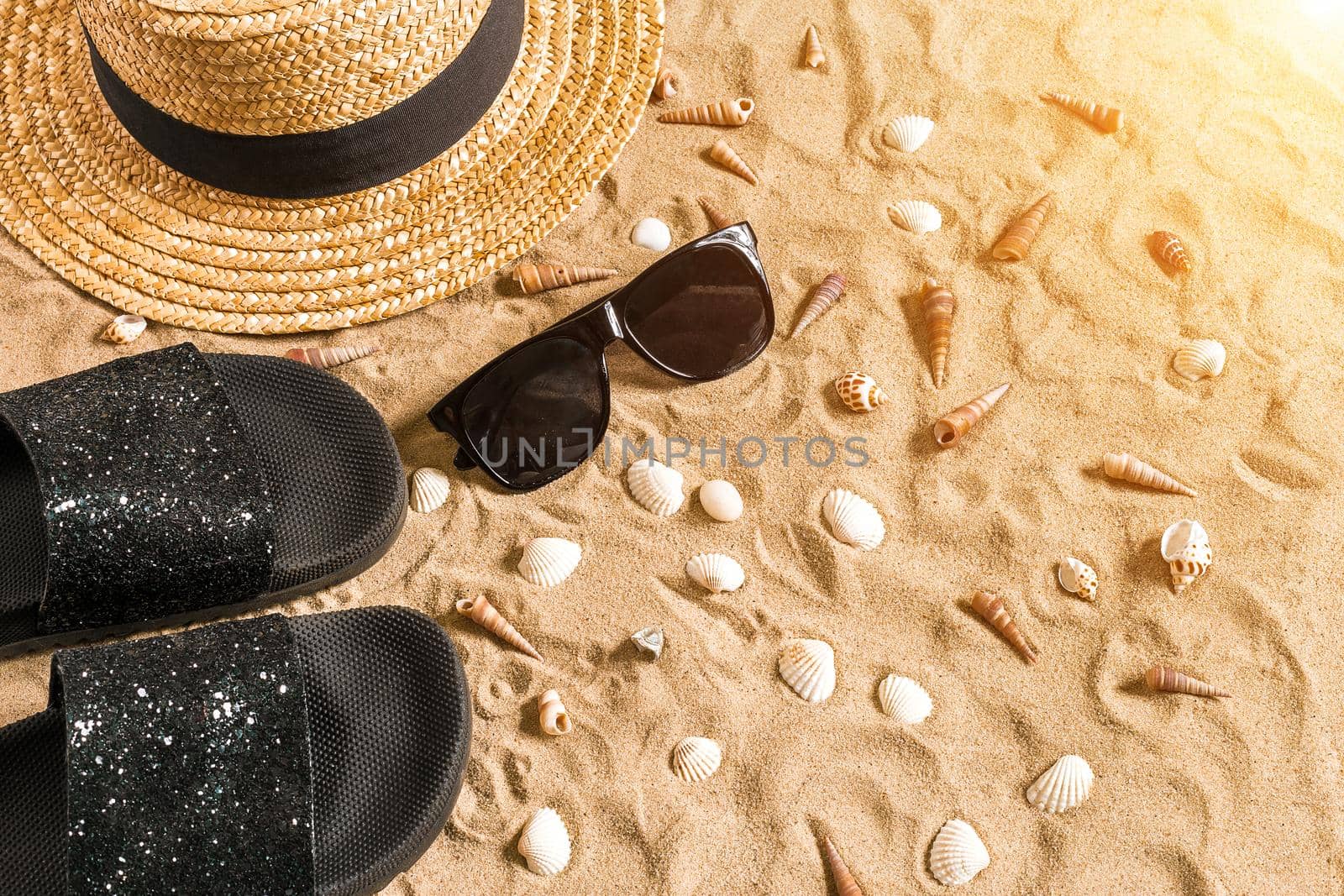 Summer beachwear, flip flops, hat, sunglasses and seashells on sand beach. Top view. Copy space. Sun flare