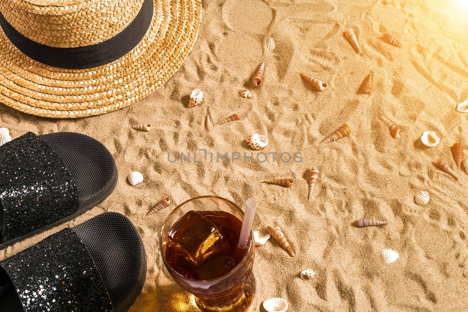 Summer beachwear, flip flops, hat, cold drink in a glass and seashells on sand beach. by nazarovsergey