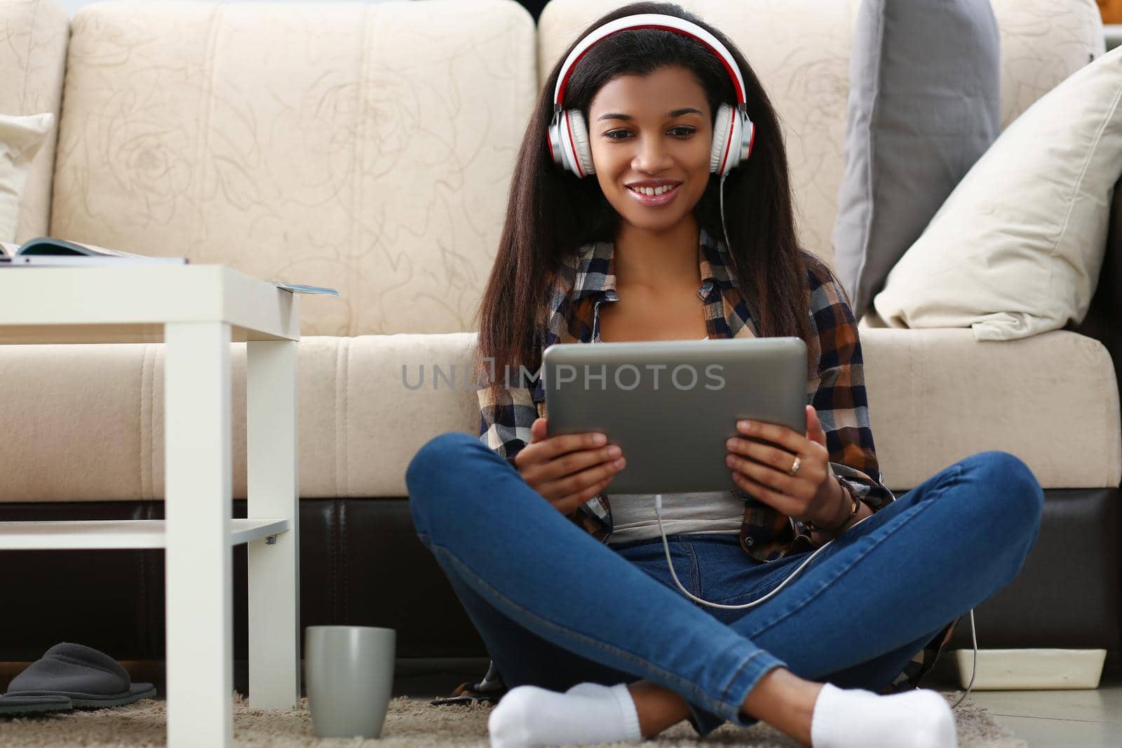 Low angle of latin young woman sit on carpet with tablet and watch show, lady in headset. Spend time at home, enjoy weekend or day off. Leisure concept