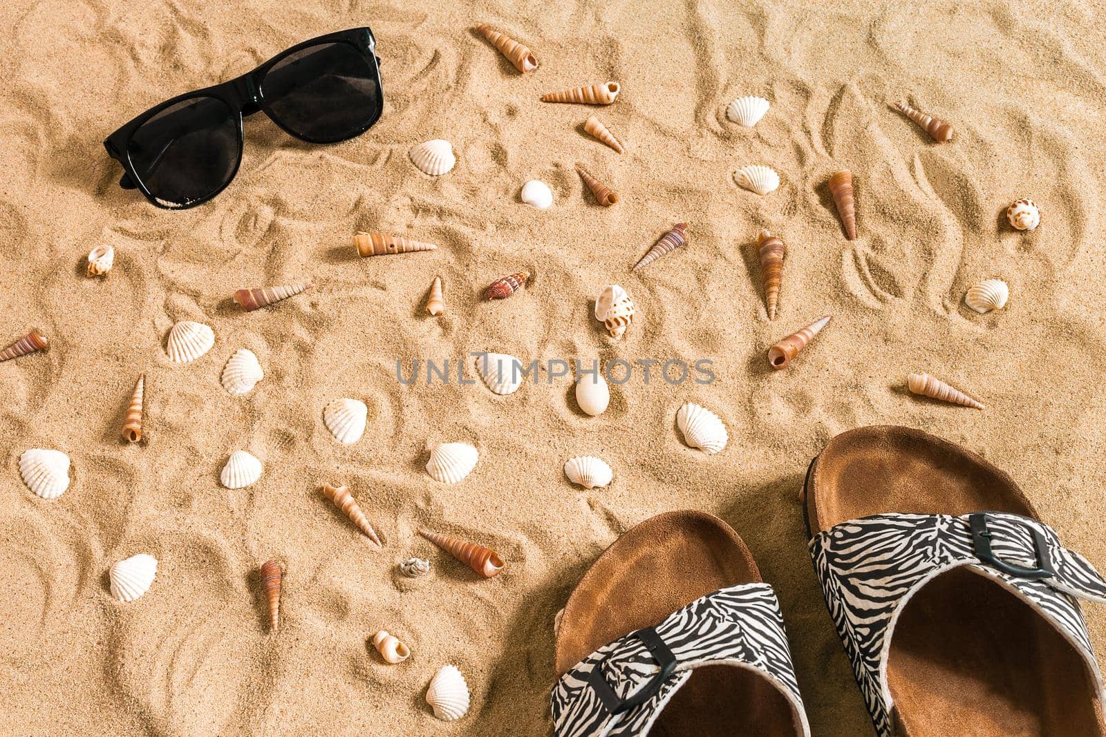 Black flip-flops and sunglass, seashell on sand. With place for your text. Top view by nazarovsergey