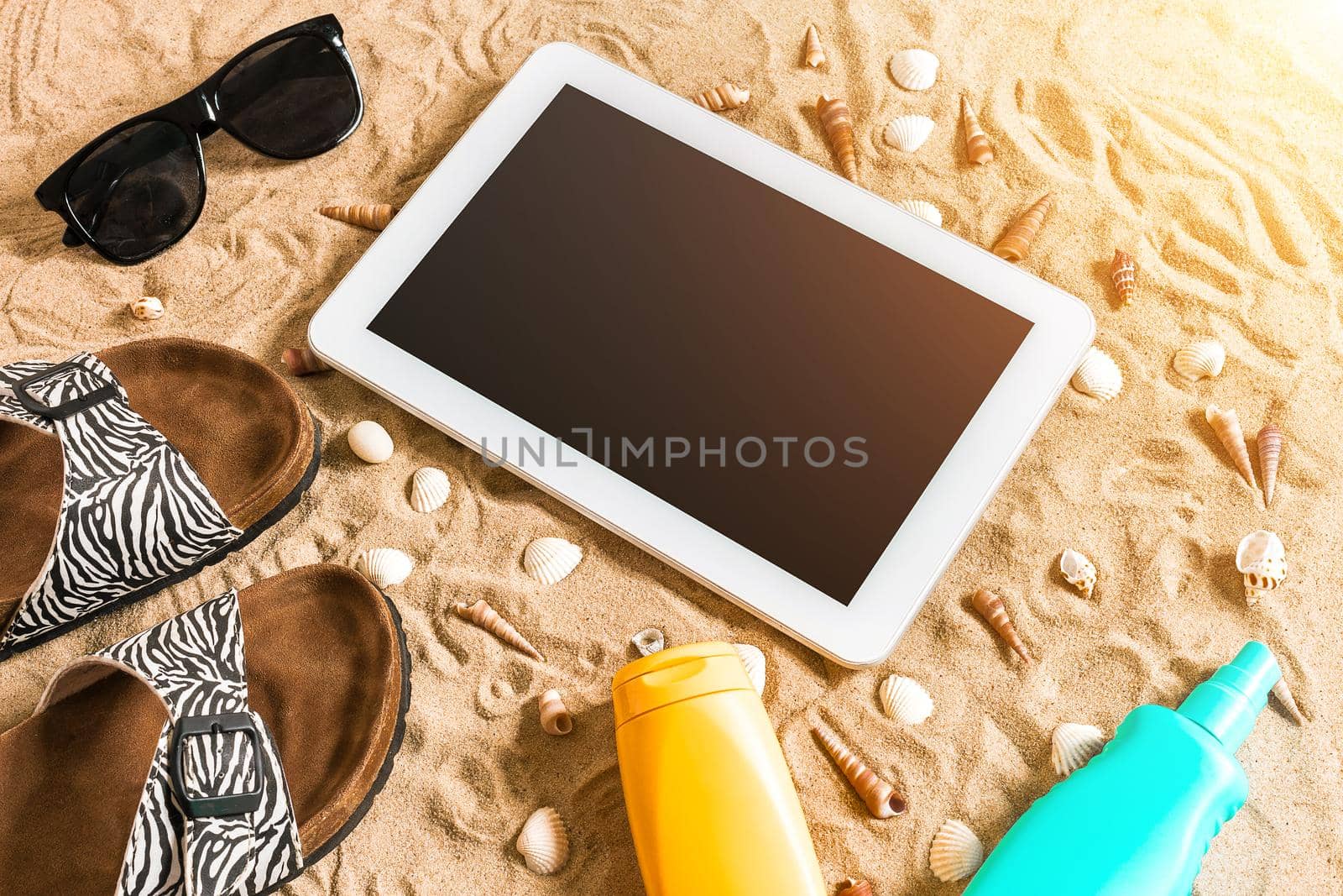 Summer flip-flops, tablet, sunglass and seashell on sand. With place for your text. Top view. Copy space. Sun flare