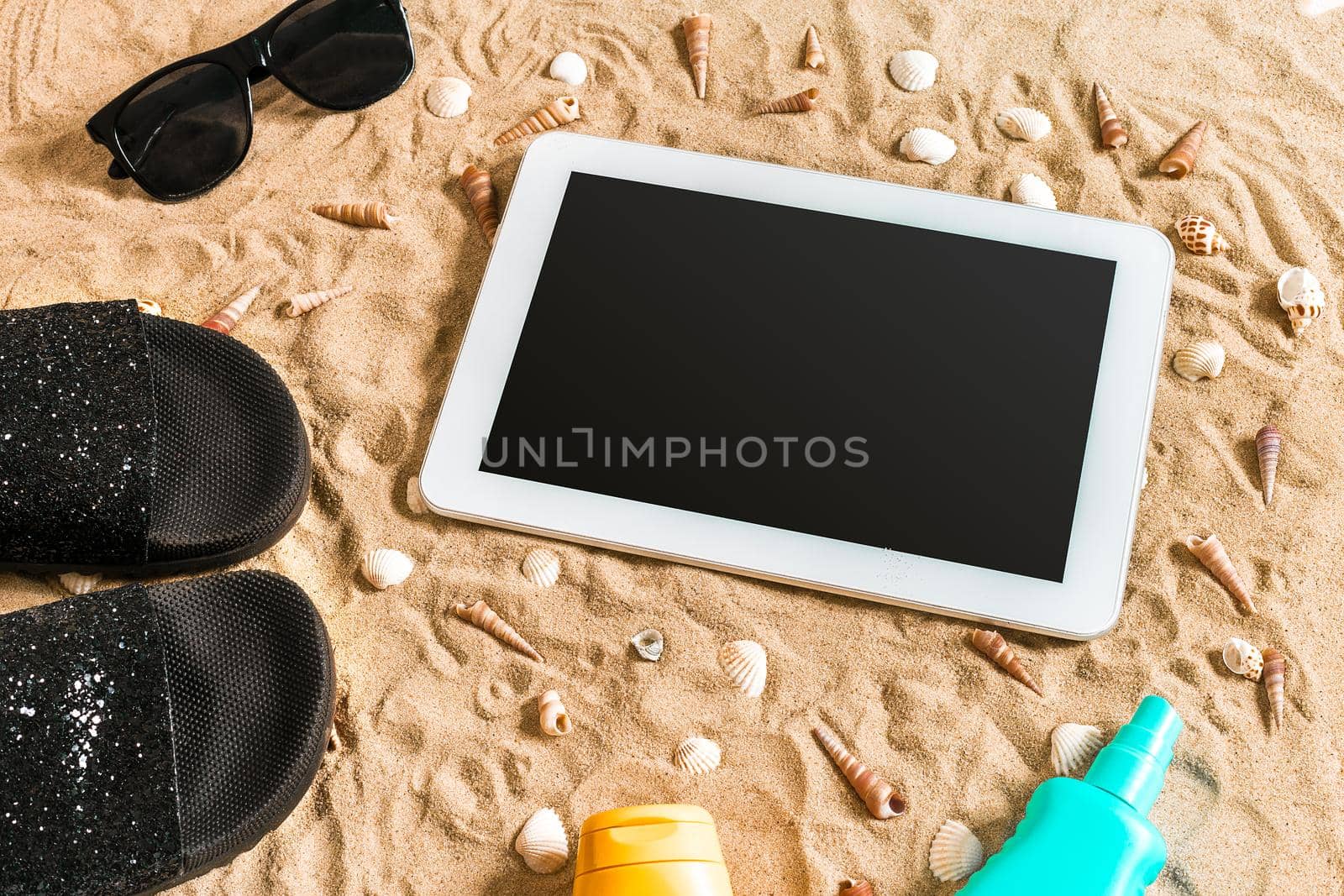 Summer flip-flops, tablet, sunglass and seashell on sand. With place for your text. Top view by nazarovsergey