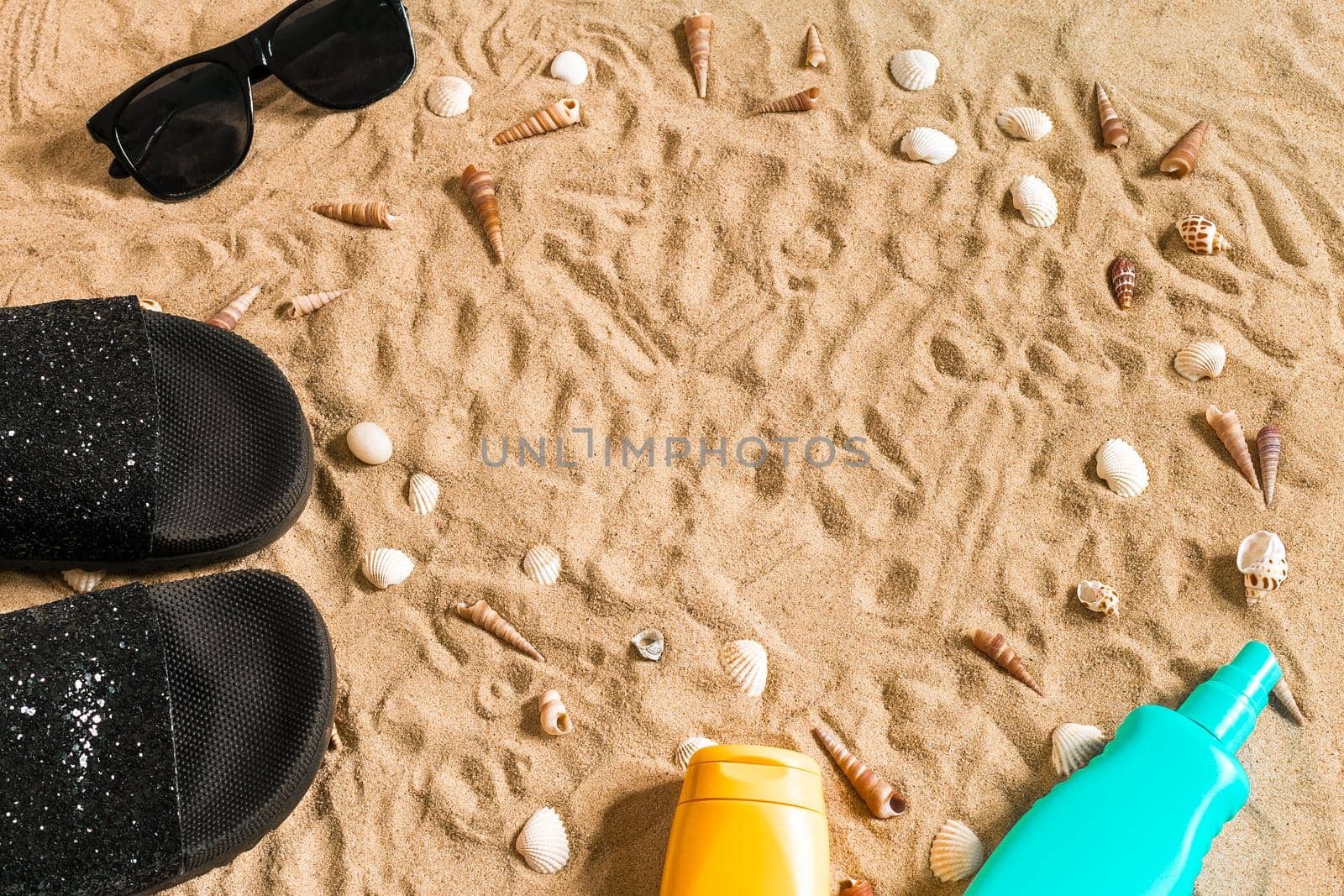 Black flip-flops and sunglass, seashell on sand. With place for your text. Top view. Copy space