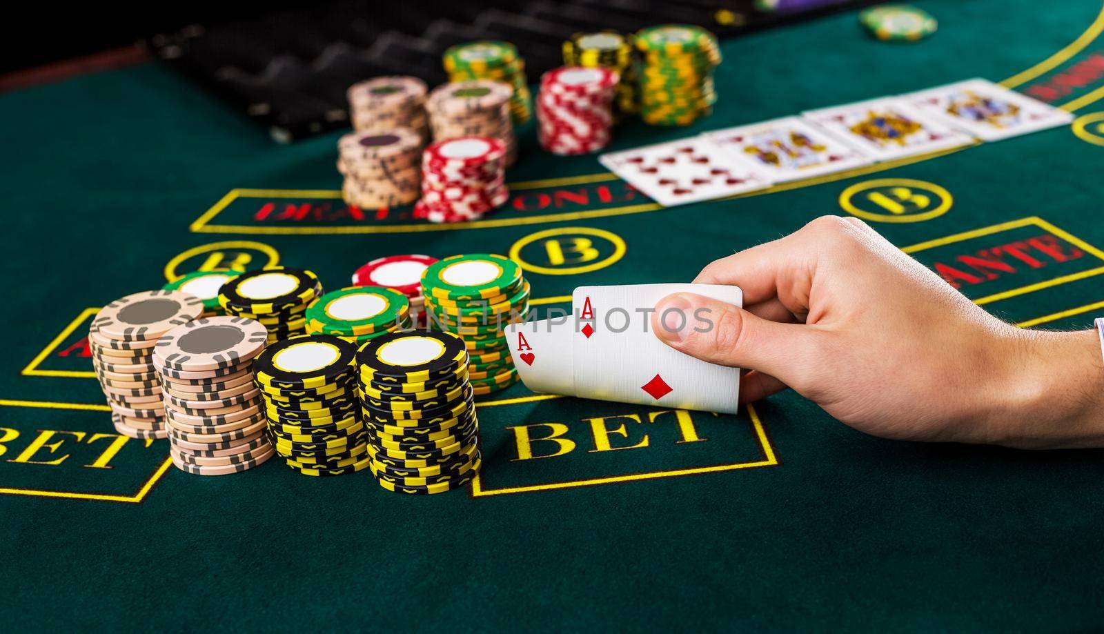 Close-up of male poker player lifting the corners of two cards aces at green casino table with aces