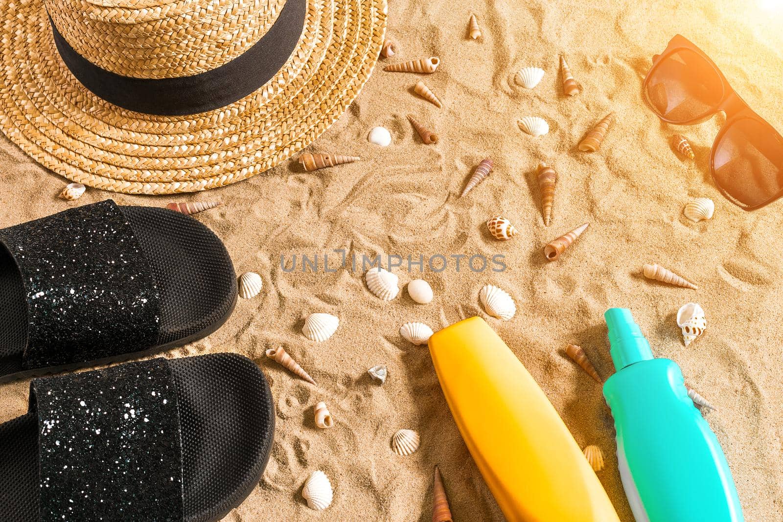 Summer beachwear, flip flops, hat, sunglasses and seashells on sand beach. Top view. Copy space. Sun flare