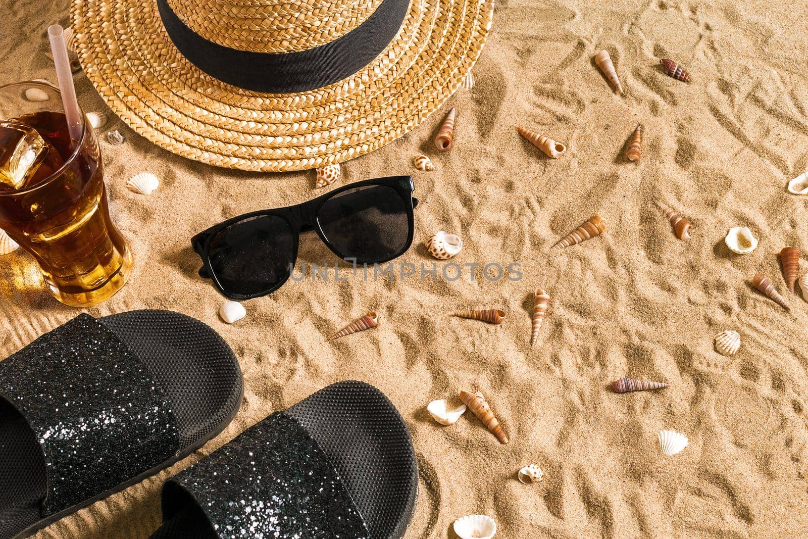 Summer beachwear, flip flops, hat, cold drink in a glass and seashells on sand beach. Top view. Copy space. Still life mockup flat lay