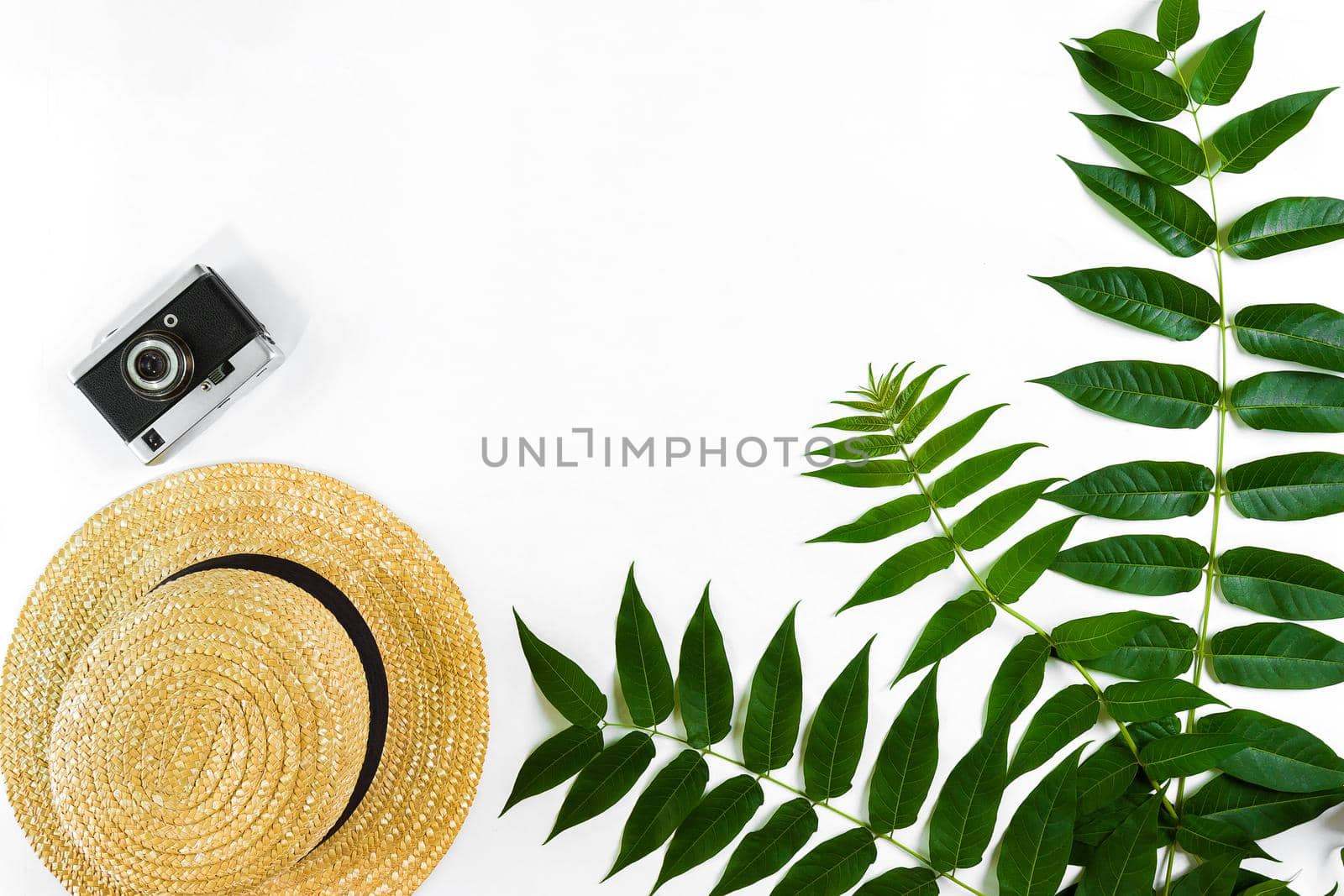 Straw hat with green leaves and old camera on white background, Summer background. Top view by nazarovsergey