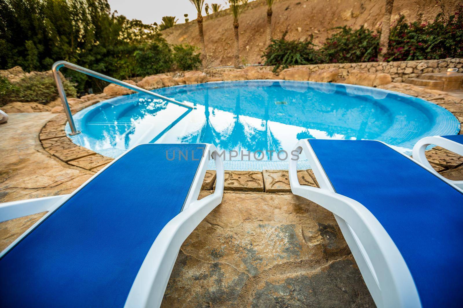 Sunloungers and beautiful swimming pool with reflected of palm trees in a blue water, Egypt.