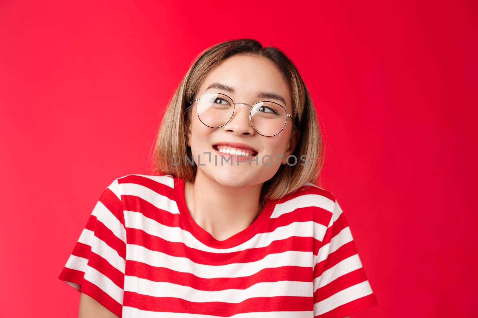 Cheerful silly cute asian girlfriend cannot wait show boyfriend b-day present smiling broadly thrilled look away pondering, thinking about pleasant happy moment, dreaming stand red background by Benzoix