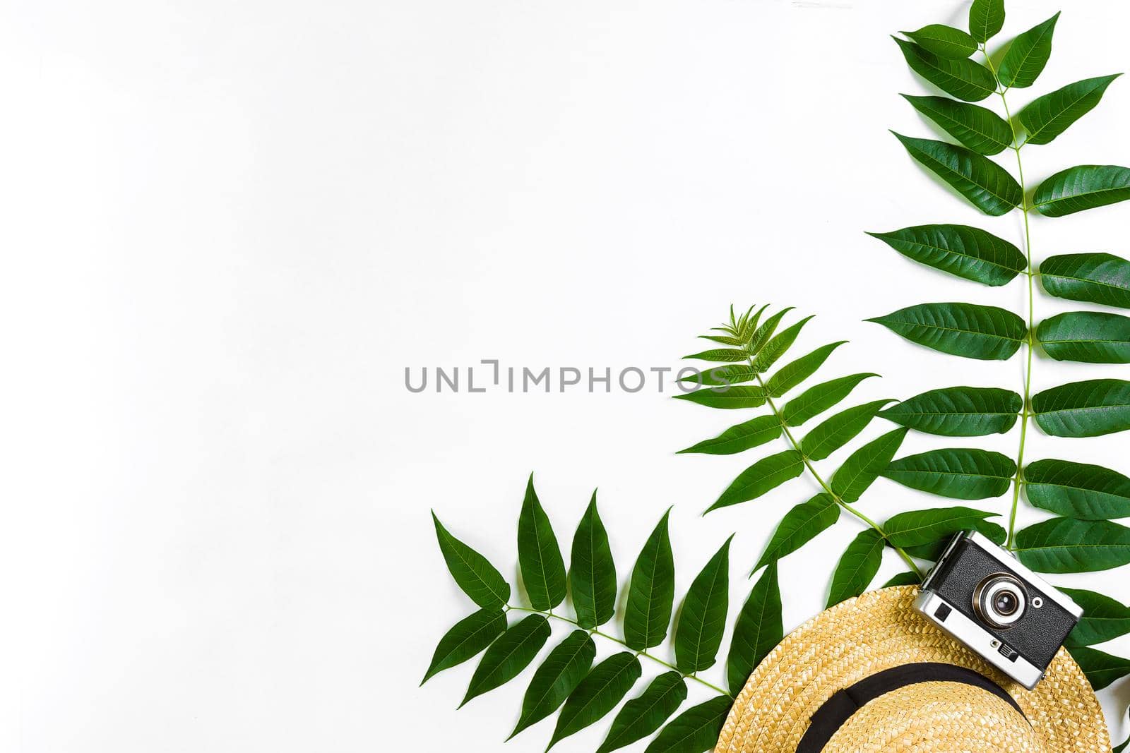Straw hat with green leaves and old camera on white background, Summer background. Top view by nazarovsergey